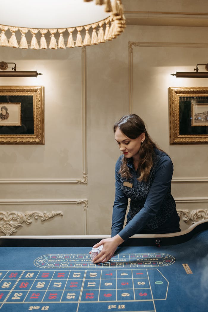 Female casino dealer managing roulette table in a luxurious setting.